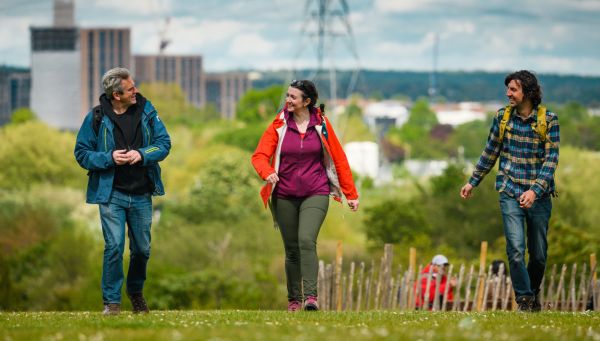 Three walkers chatting on a walk with buildings and a pylon in the background